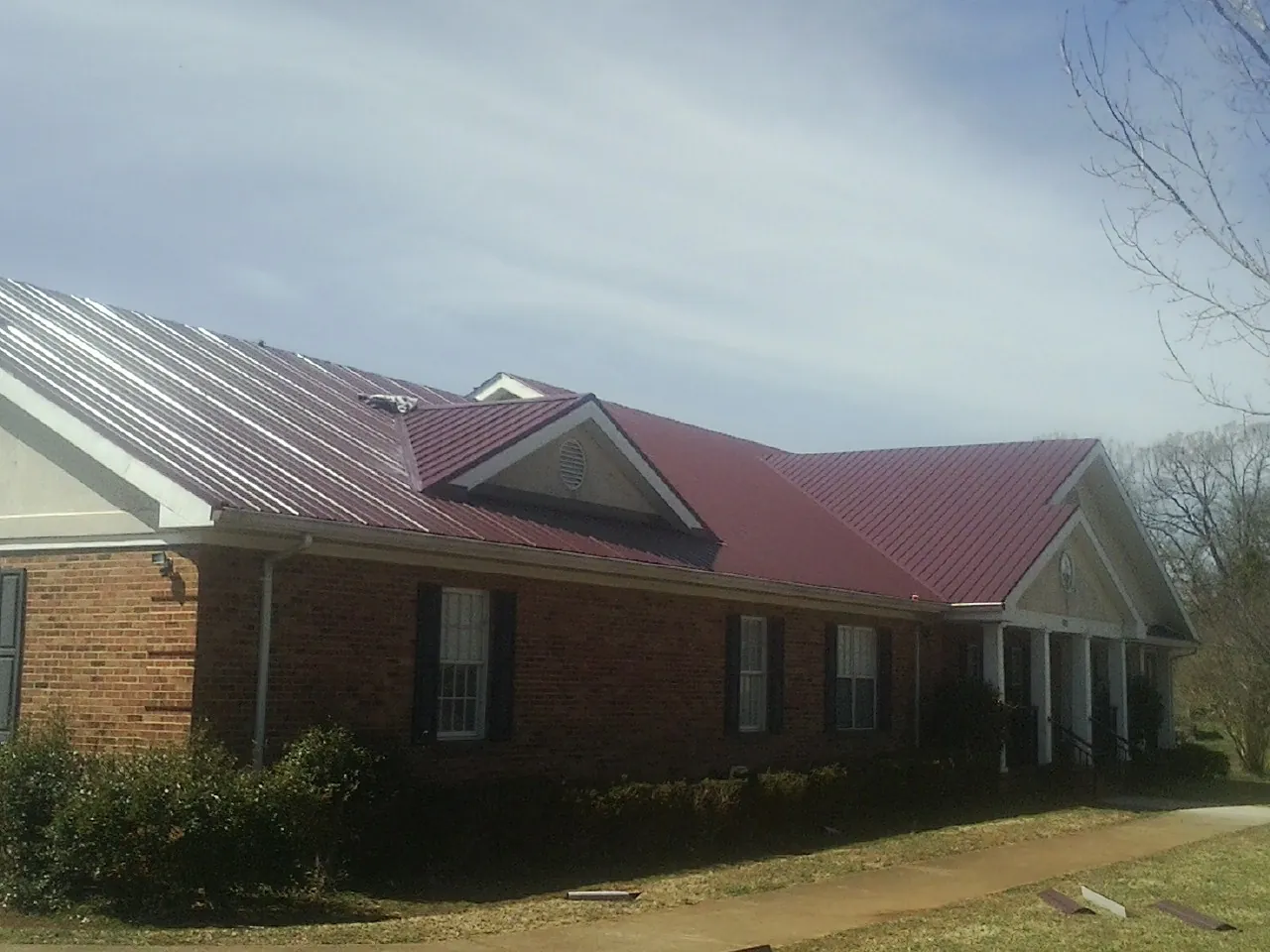 Red metal roof with gabled entries on a long brick building, from a Hail Damage Roof Repair job in Pembroke Township