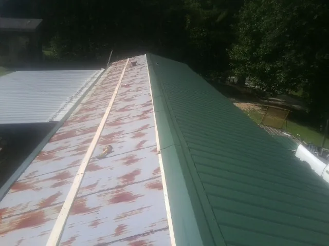 Old rusted panels beside newly installed green metal roofing — Wind Damage Roof Repair by Roofing Brothers in Pembroke Township