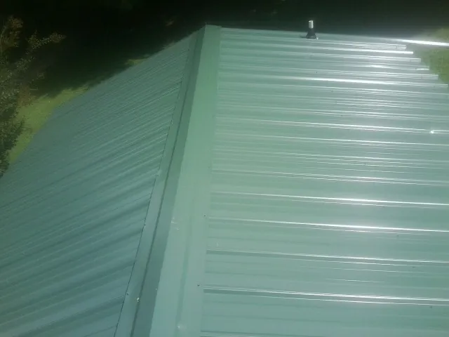 New green metal panels meeting at the ridge of a roof — Flat Roof Repair work by our crew in Pembroke Township