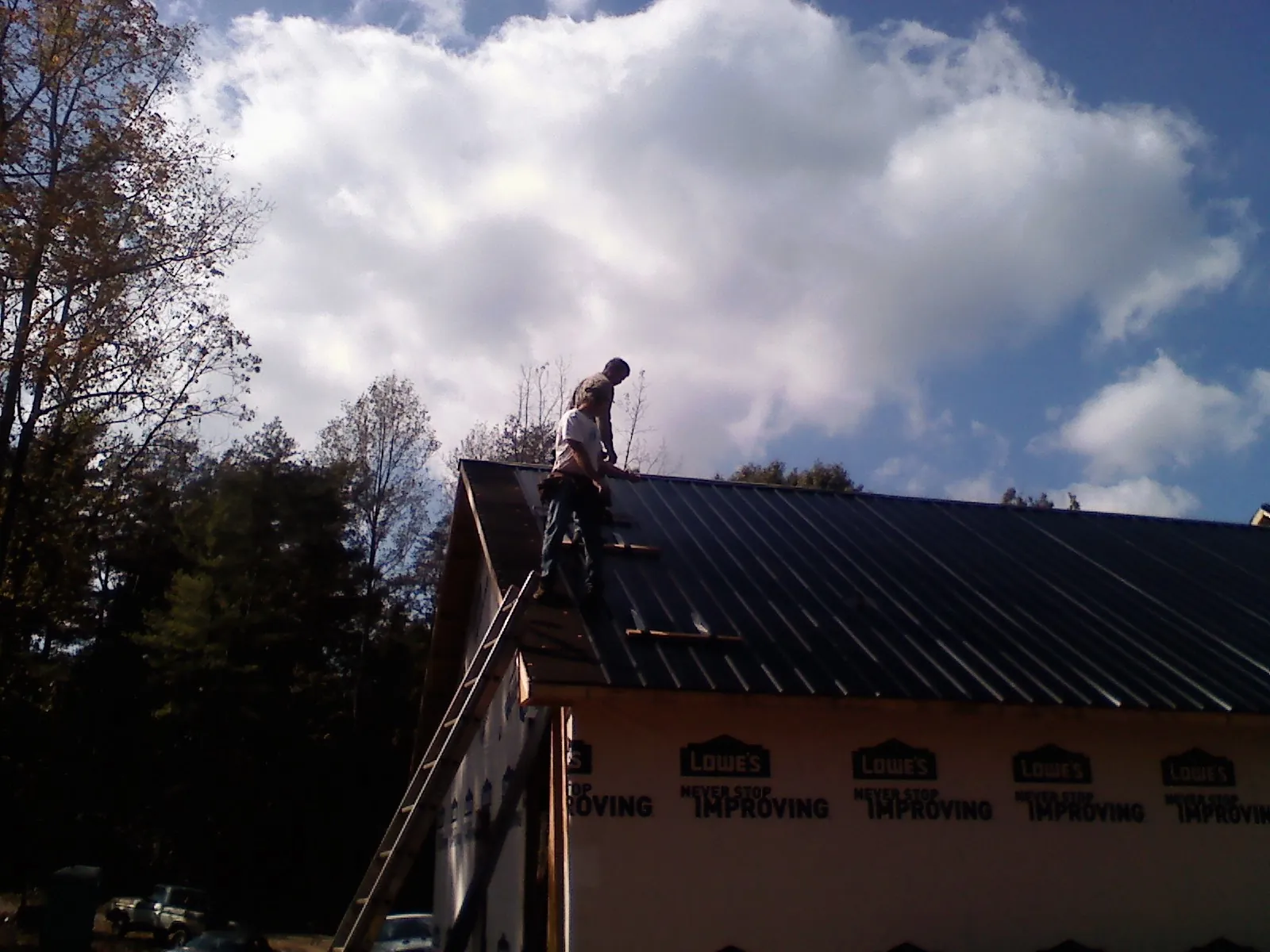 Roofer fastening dark metal panels high against a cloudy sky, from a Roof Inspection job in Pembroke Township