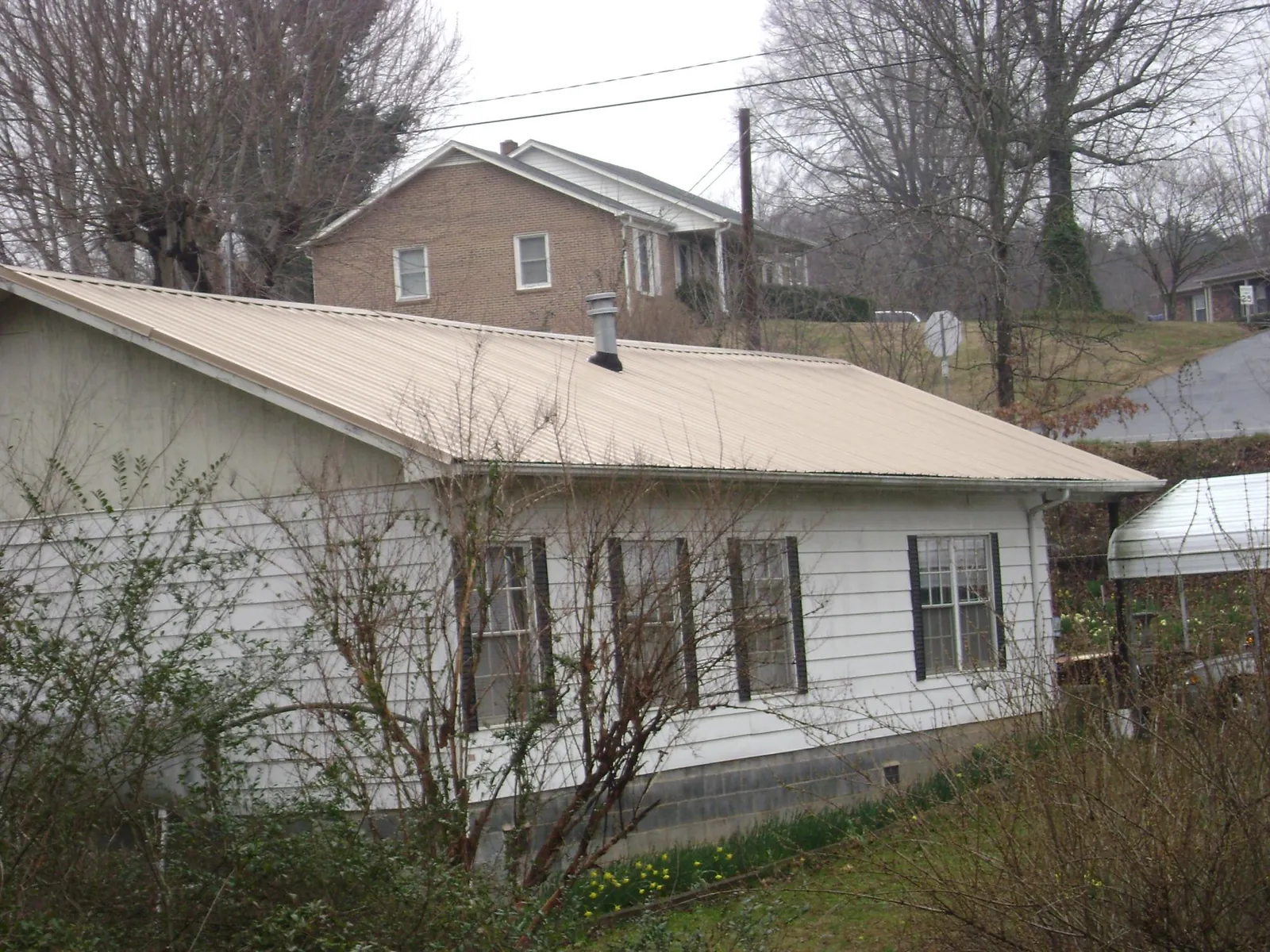 Tan metal roof on a white sided house set into a hillside — Commercial Roofing by Roofing Brothers in Pembroke Township