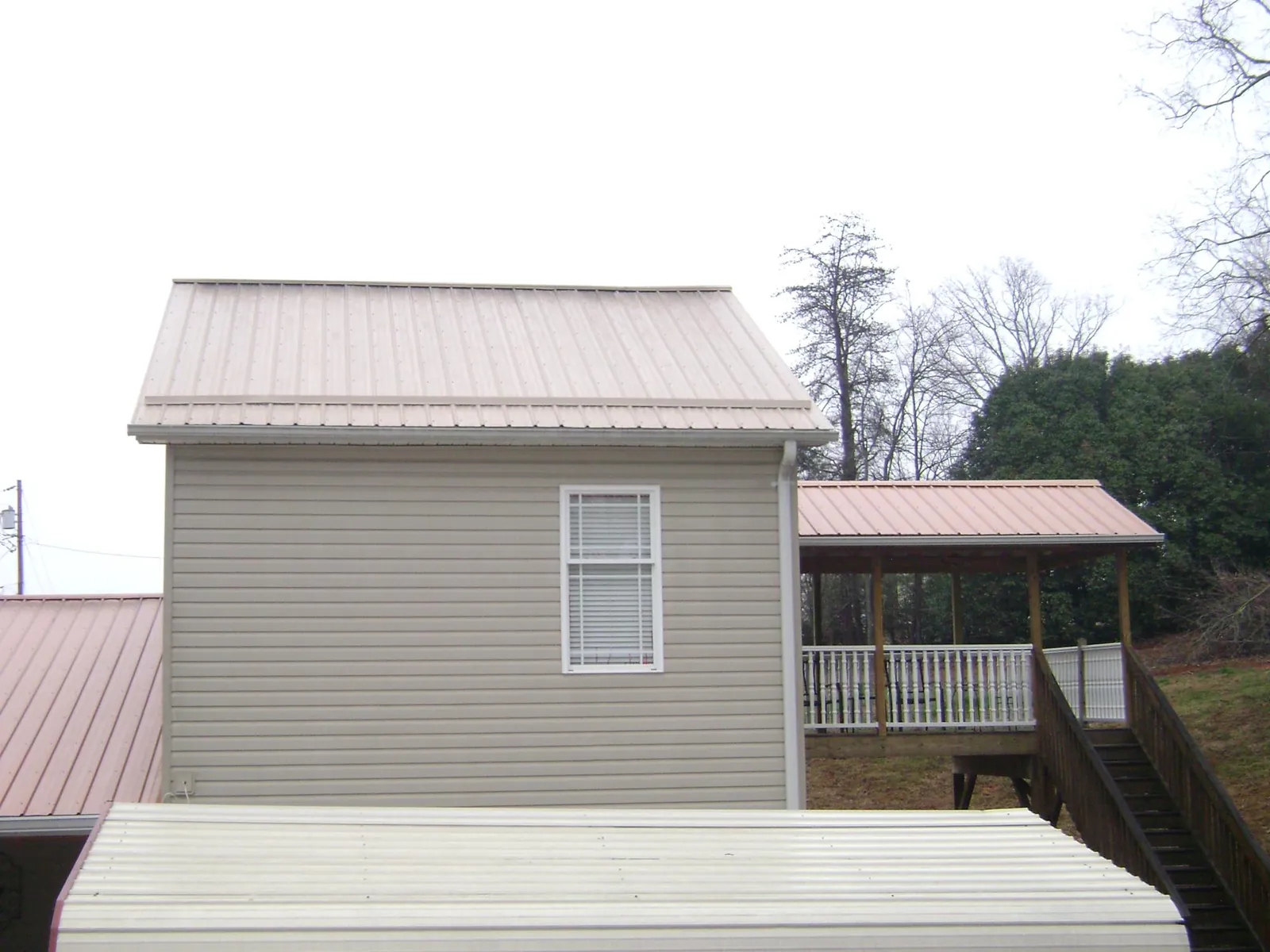 Tan metal roofs on a two story addition and attached porch, from a Roof Replacement job in Pembroke Township